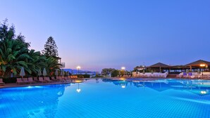 A swimming pool with lounge chairs and umbrellas, surrounded by greenery and a building with a roofed area. - Apollonia Beach Resort & Spa (Malevizi)