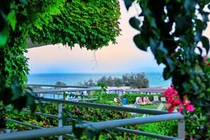 A balcony with a view of the sea, surrounded by greenery and a railing. - Apollonia Beach Resort & Spa (Malevizi)