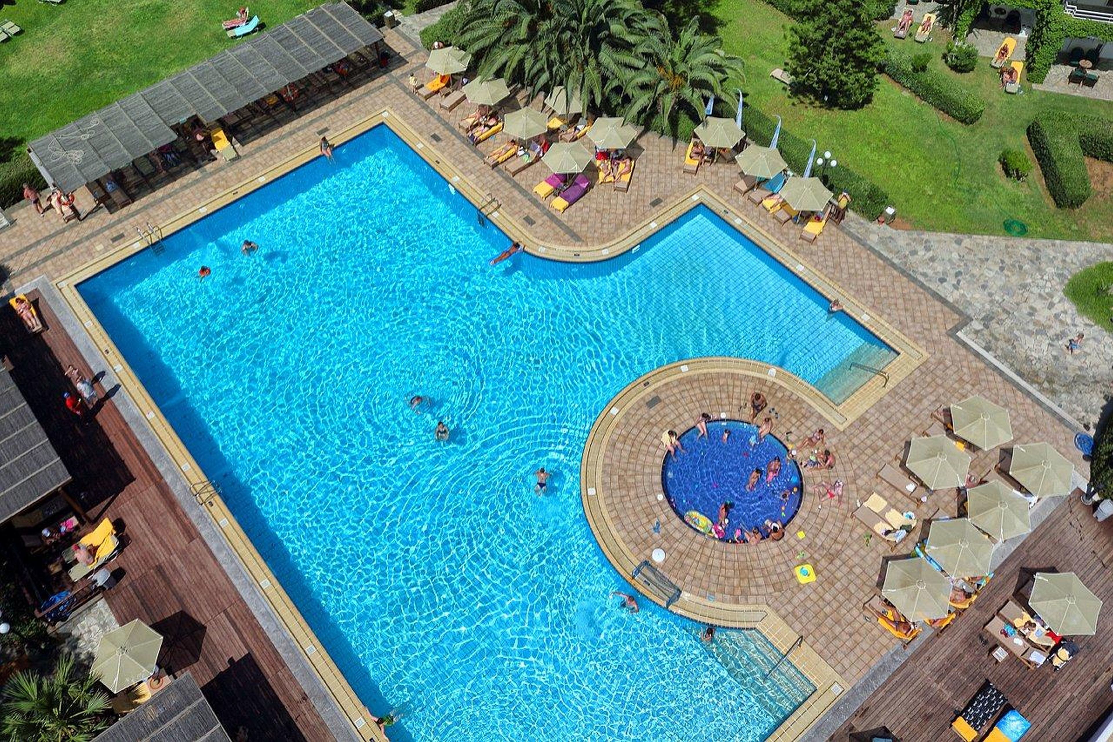 A large rectangular swimming pool with a circular hot tub area, surrounded by lounge chairs and umbrellas.