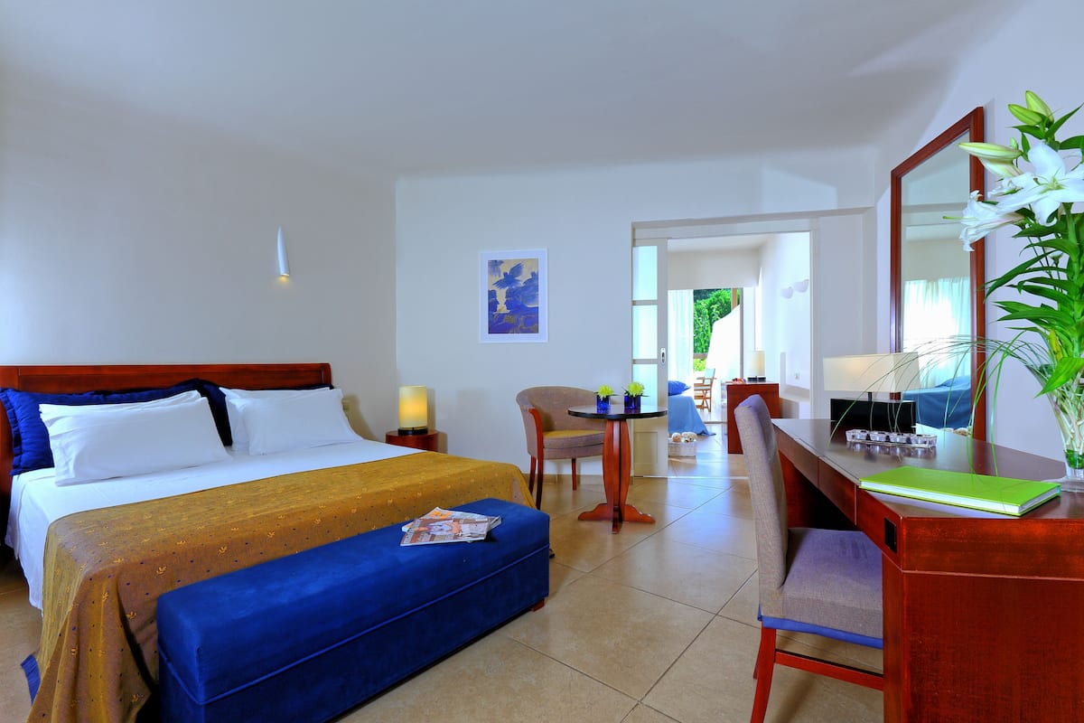 A hotel room with a bed, a desk, a chair, and a bench.