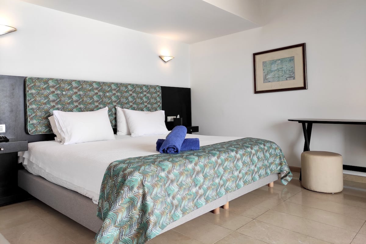 A neatly made bed with a patterned bedspread, a bedside table with a lamp, and a framed picture on the wall.
