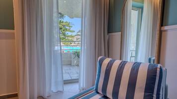 A room with a view of a pool, a striped pillow on a sofa, and sheer curtains.