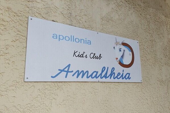 A sign with the text 'apollonia Kids Club Amaltheia' and a partial image of a white horse. - Apollonia Beach Resort & Spa (Malevizi)