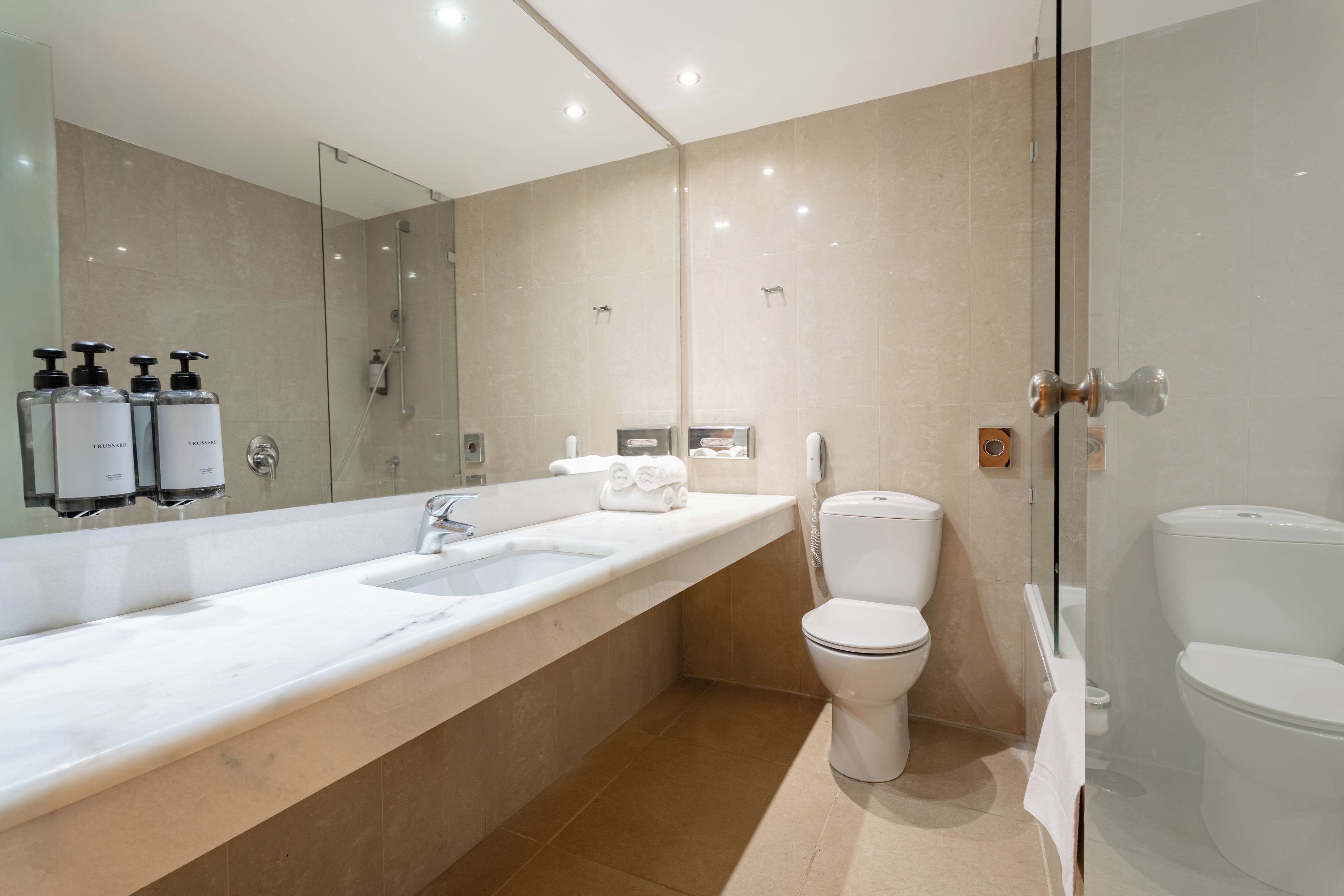 Une salle de bain moderne avec un long meuble-lavabo, une douche et deux toilettes.