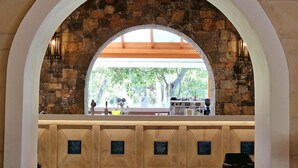 A stone archway leading to a bar area with a stone wall backdrop and a view of the outdoors. - Apollonia Beach Resort & Spa (Malevizi)