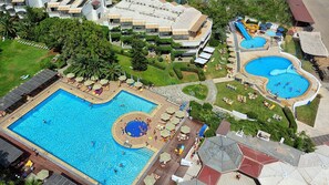 Vista aérea de un complejo turístico con múltiples piscinas, tumbonas y un jardín bien cuidado.