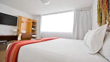 Habitación de hotel con cama, televisor en la pared, escritorio con silla y armario.