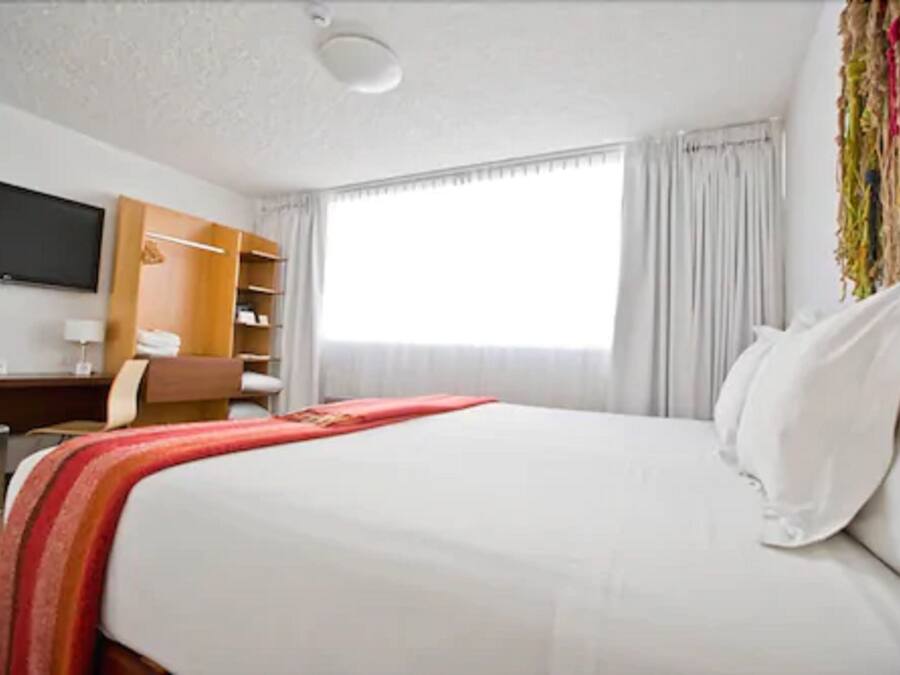 Habitación de hotel con cama, televisor en la pared, escritorio con silla y armario.