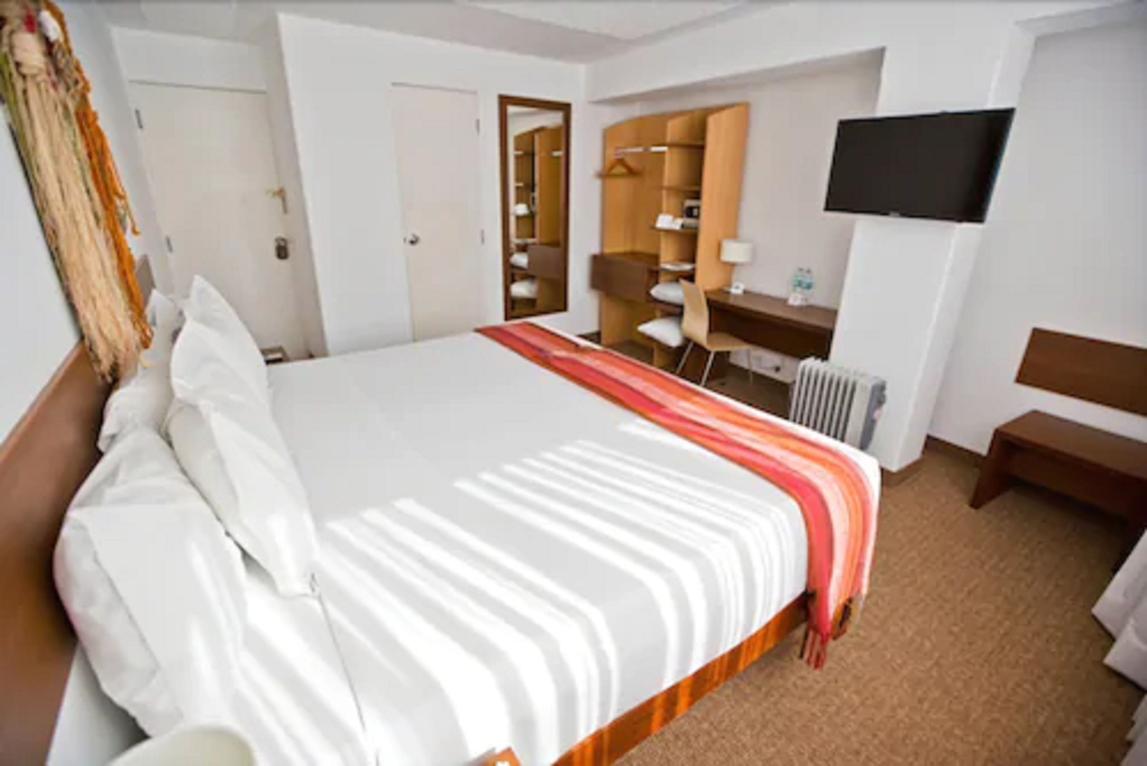 Una habitación de hotel con una cama grande, un escritorio, una silla, un televisor y un armario.