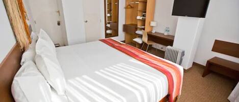 Una habitación de hotel con una cama grande, un escritorio, una silla, un televisor y un armario.