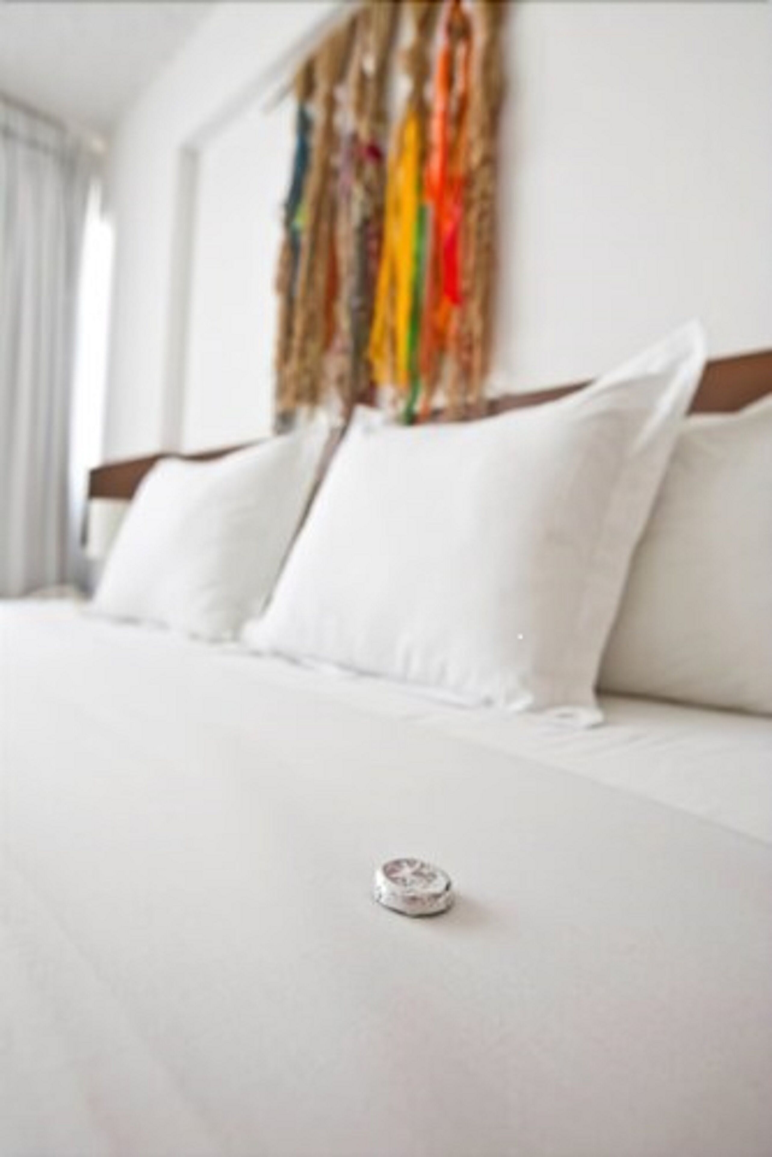A hotel room with a bed, white bedding, and a colorful abstract painting on the wall.