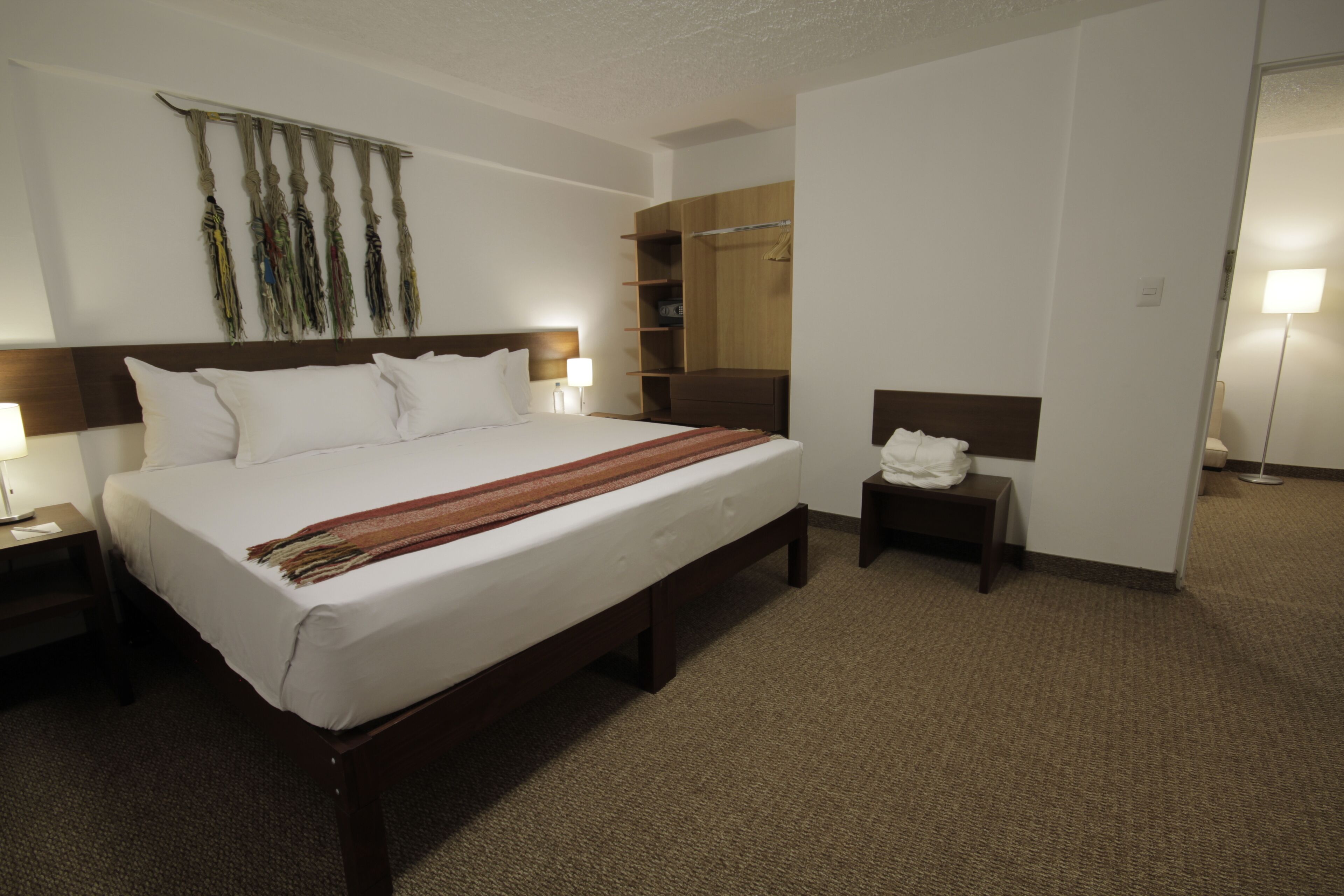 A hotel room with a large bed, a bedside table with a lamp, a wardrobe, and a mirror.