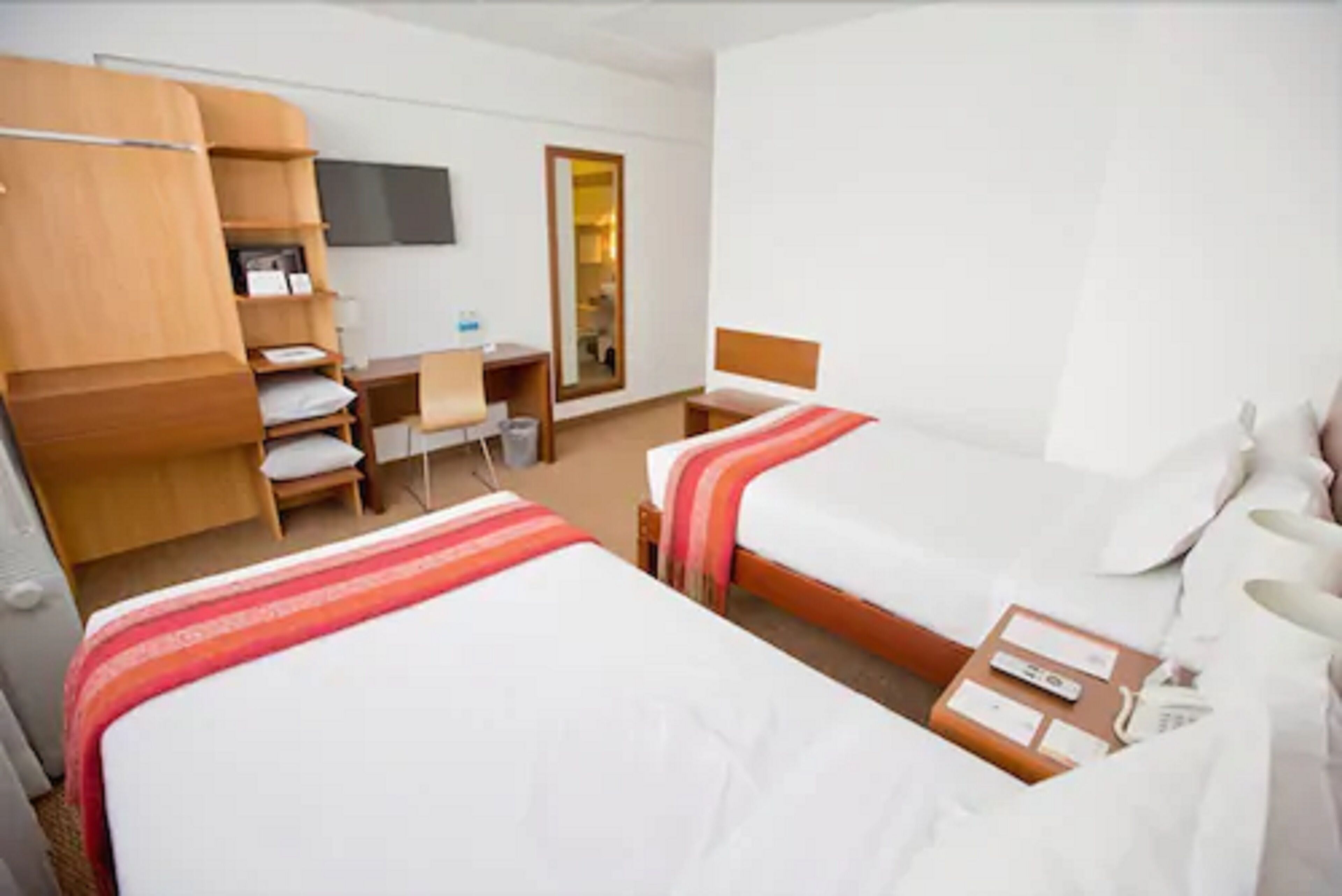 A hotel room with two beds, a desk, a chair, a TV, and a wardrobe.