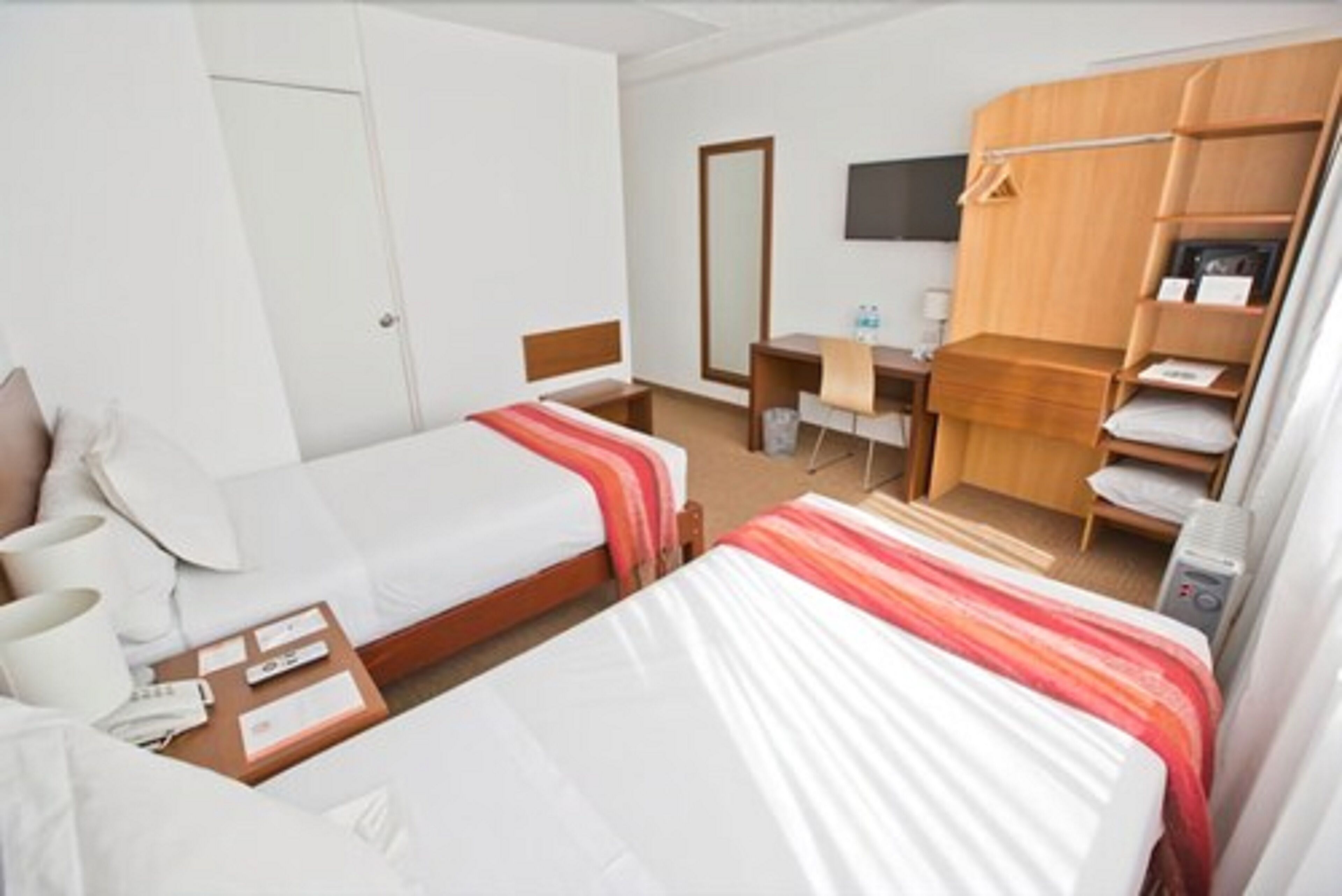 A hotel room with two beds, a desk, a chair, a wardrobe, and a television.