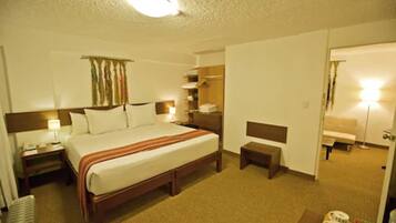 A hotel room with a large bed, bedside tables, a nightstand, a bench, a wardrobe, and a mirror.