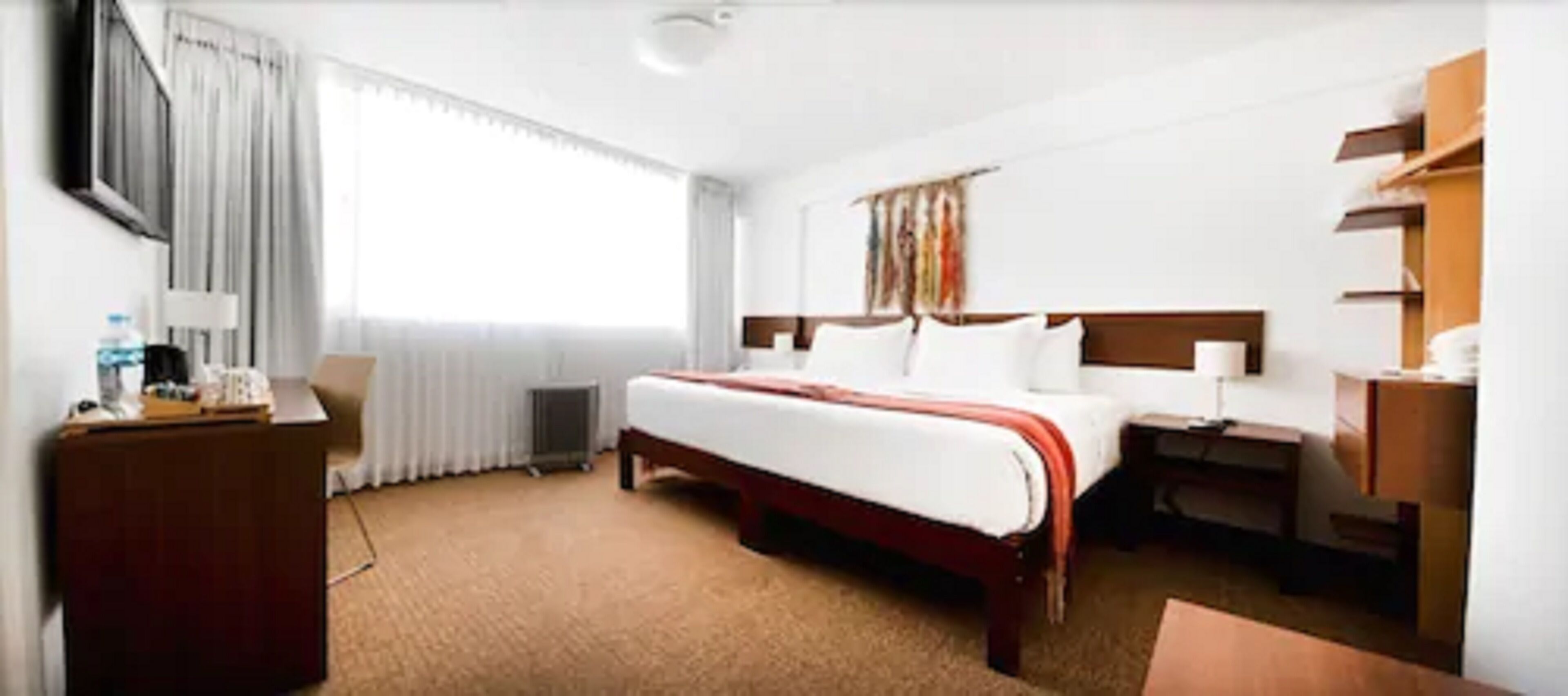A hotel room with a bed, bedside tables, a desk, and a window with curtains.
