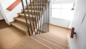 Un escalier recouvert de moquette, doté d’une main courante en bois et de balustres noires.