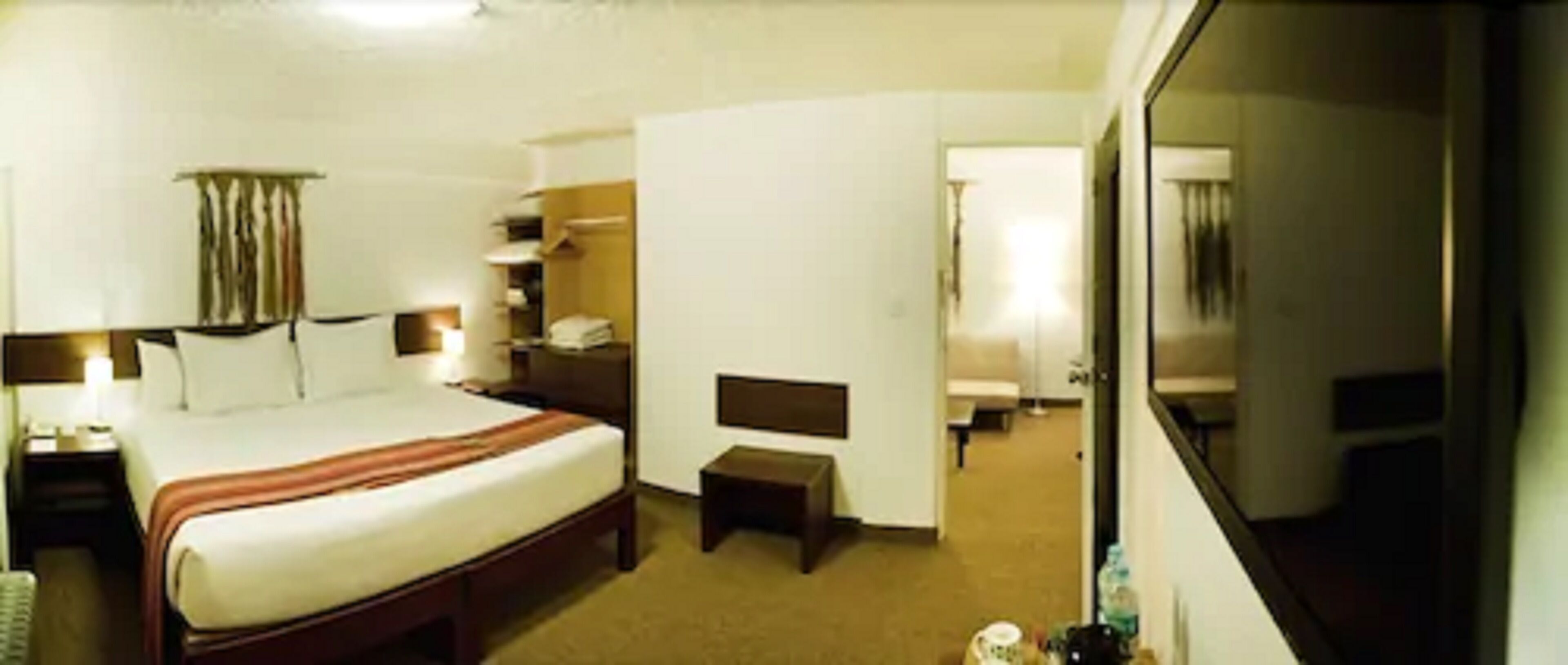 A hotel room with a bed, a small table, a chair, a desk, and a mirror.