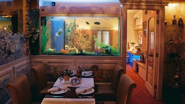 A dining area with a large aquarium, a table set for two, and a bar area in the background. - Boutique Palace Hotel Baku (Baku)