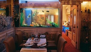 Un espace repas agrémenté d’un grand aquarium, une table dressée pour deux personnes et un bar en arrière-plan.