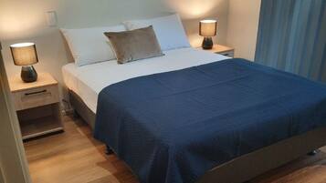 A neatly made bed with a blue bedspread, two bedside lamps, a nightstand, and a wall-mounted picture.