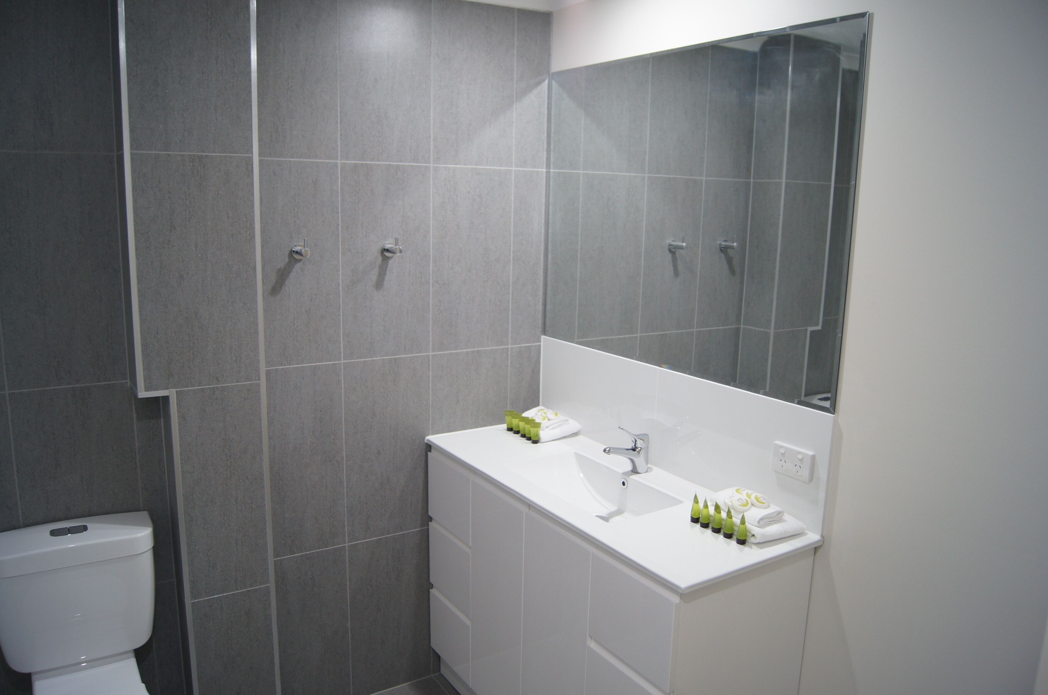 Un baño moderno con baldosas grises, un lavabo blanco y un espejo grande.