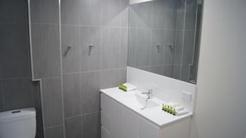 Un baño moderno con baldosas grises, un lavabo blanco y un espejo grande.
