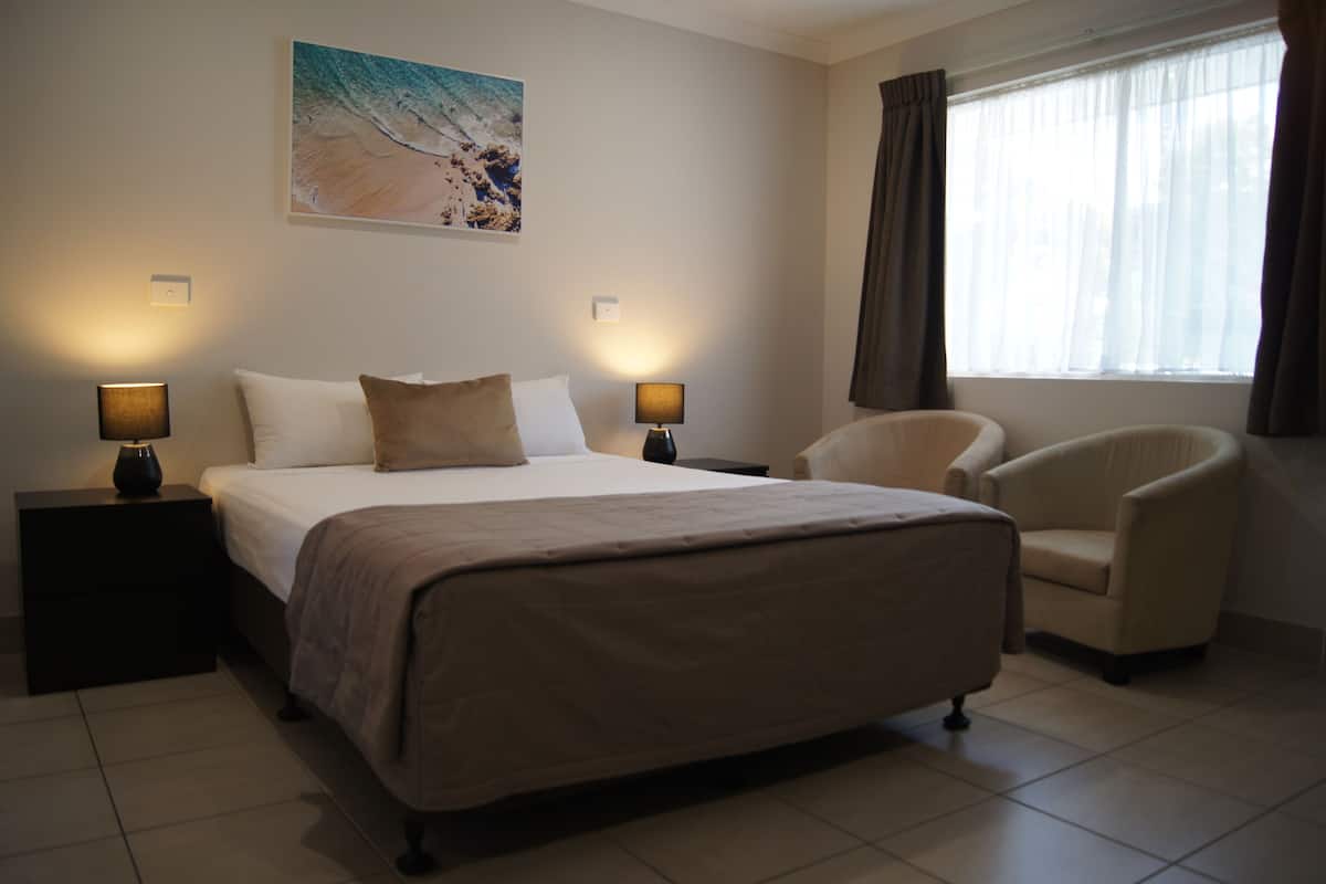 Une chambre d’hôtel avec un grand lit, deux tables de chevet avec des lampes, une chaise et une fenêtre avec des rideaux.