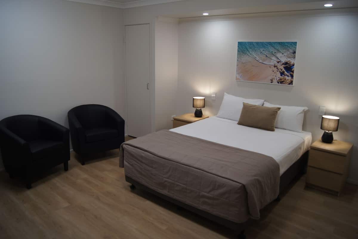 Une chambre à coucher avec un lit, deux chaises, une table de chevet avec une lampe et un tableau au mur.