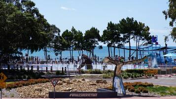 A public park with a whale sculpture, a sign reading "#Whalesherveybay", and a view of the sea.