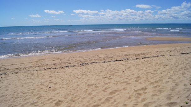 Uma praia com céu limpo e águas calmas.