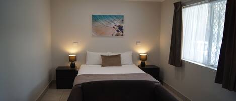 Habitación de hotel con una cama, dos mesitas de noche con lámparas, un cuadro grande en la pared, una ventana con cortinas y un sofá.