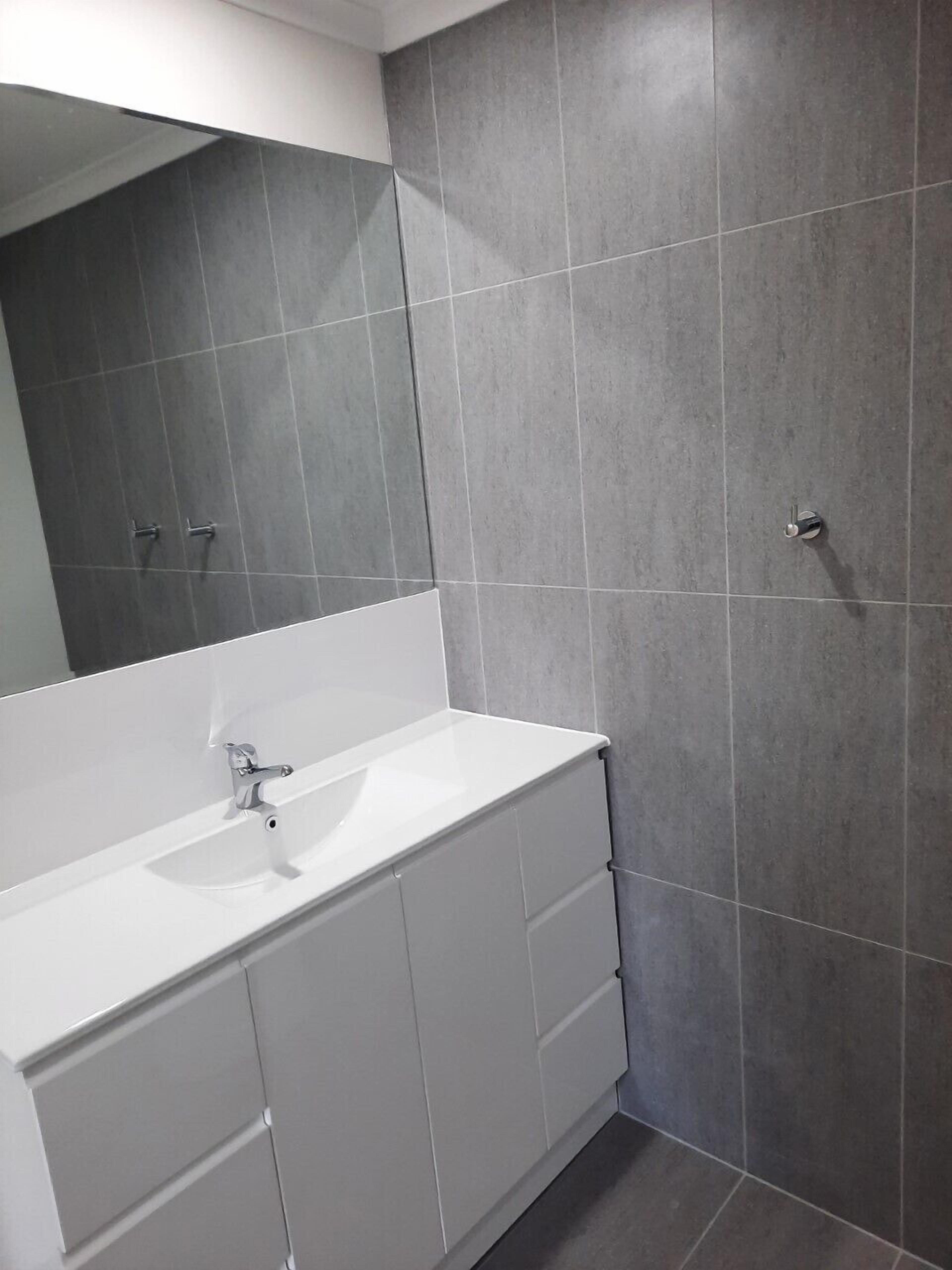 A bathroom with a white vanity, a mirror, and grey tiled walls.