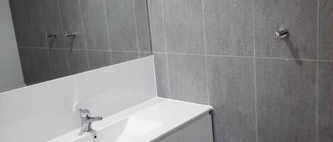 A bathroom with a white vanity, a mirror, and grey tiled walls.