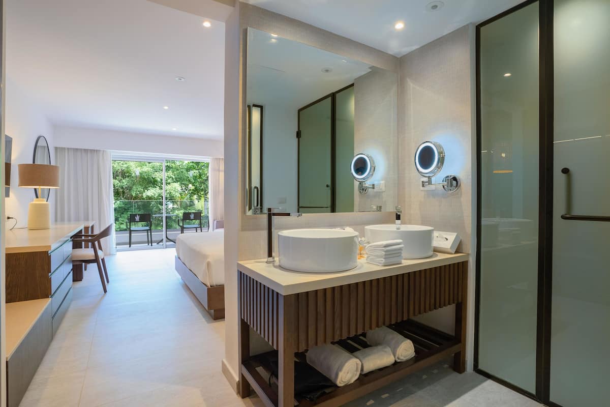 A modern hotel bathroom with a large mirror, two sinks, and a shower area.