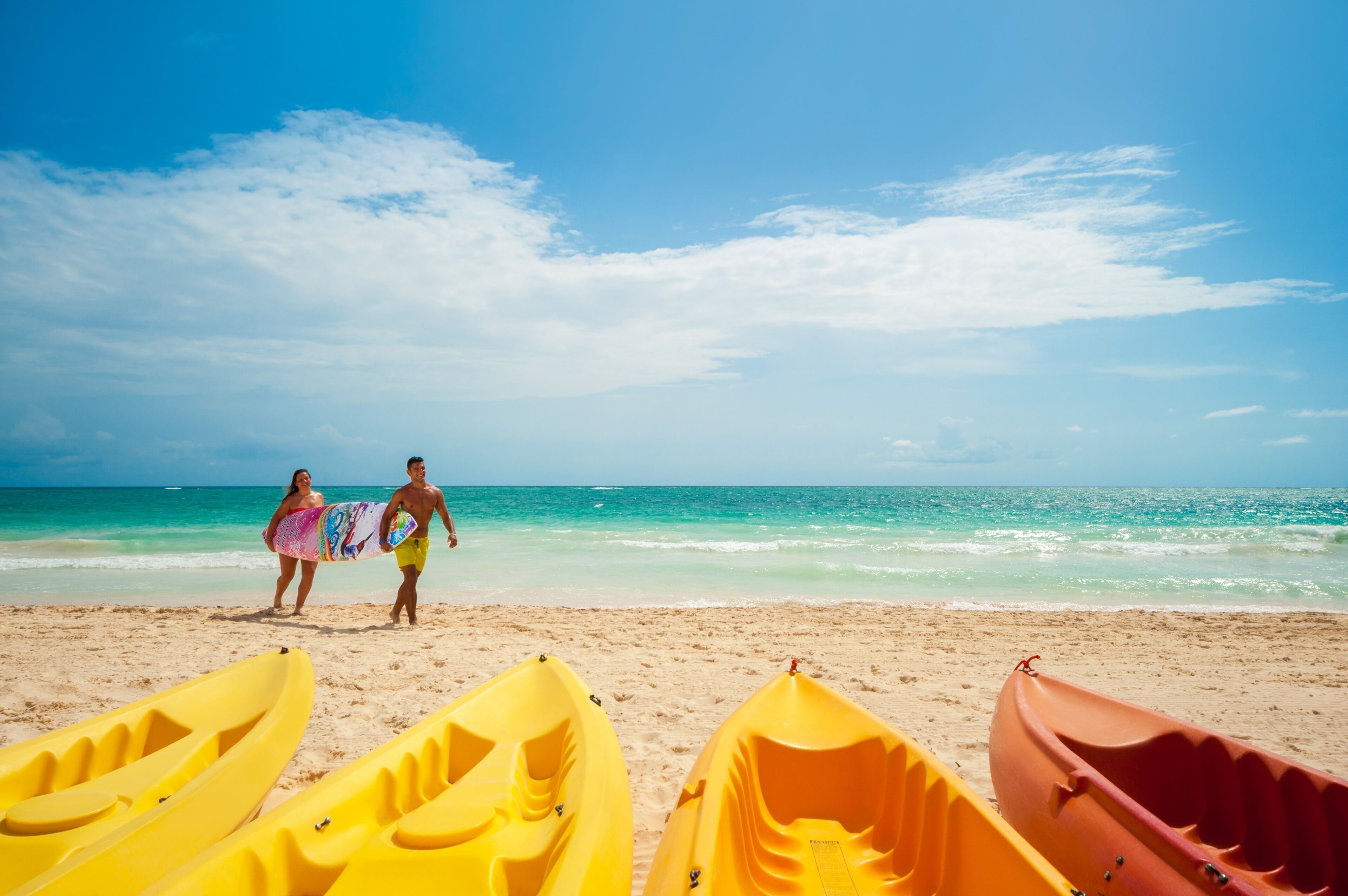 A beach with kayaks and a couple walking on the sand.