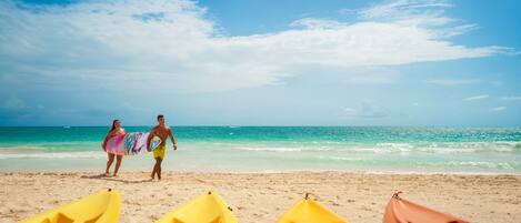 A beach with kayaks and a couple walking on the sand.