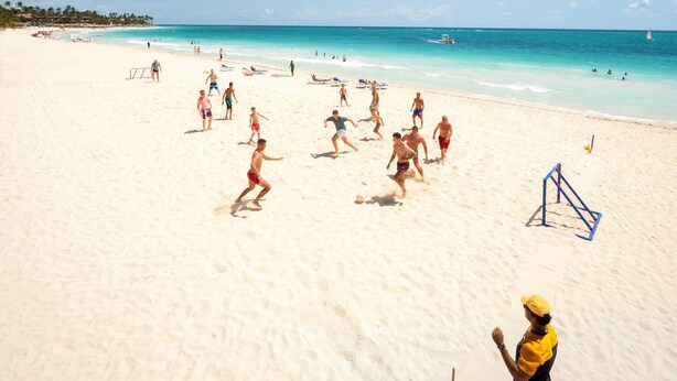 Een zandstrand met mensen die volleybal spelen en een paraschutist in de lucht.