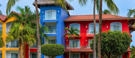 A colorful hotel with a blue building, red building, and a yellow building. There are palm trees and a well-maintained lawn.