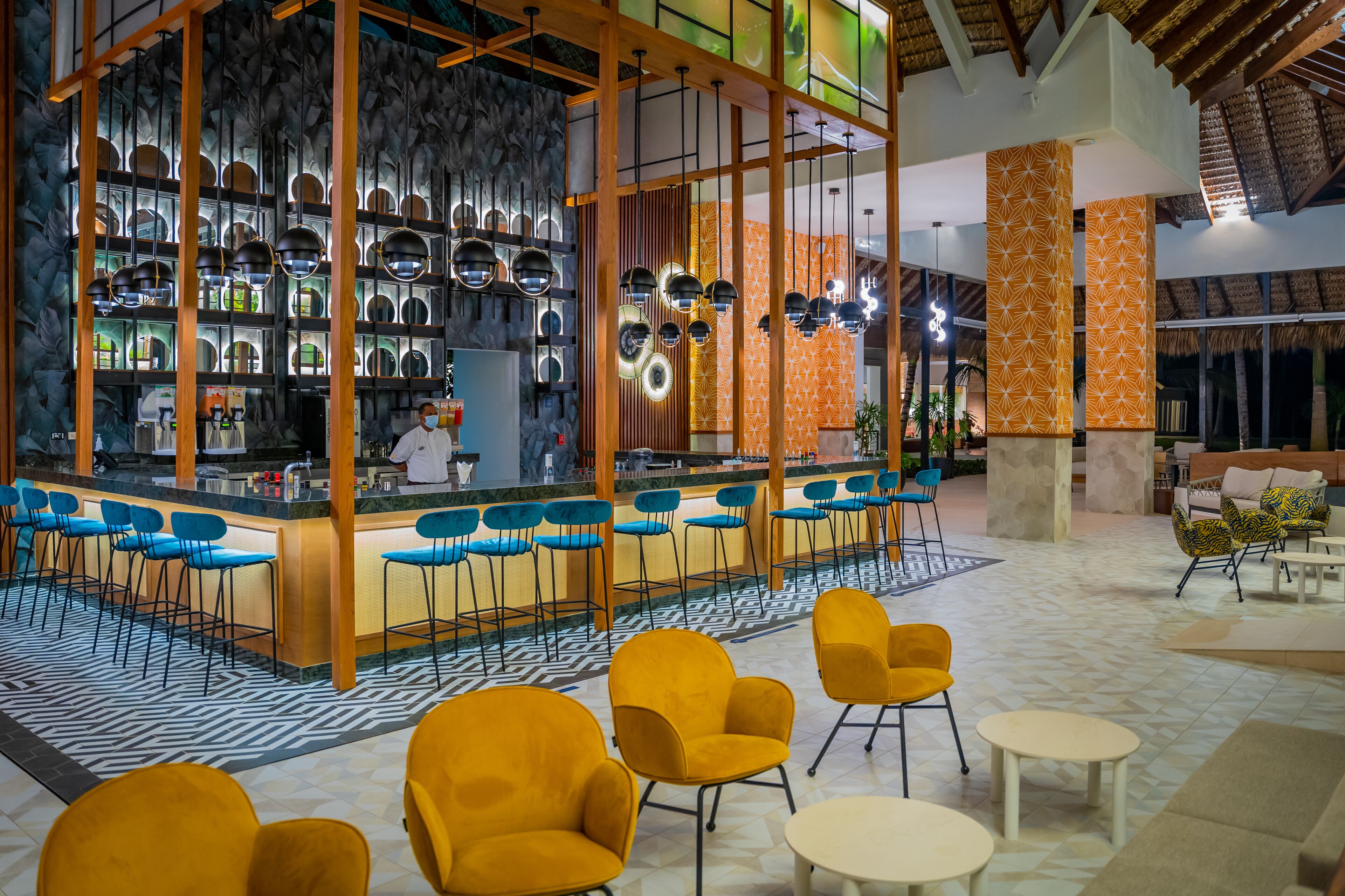 A modern bar area with a counter, blue and yellow chairs, and a patterned floor.