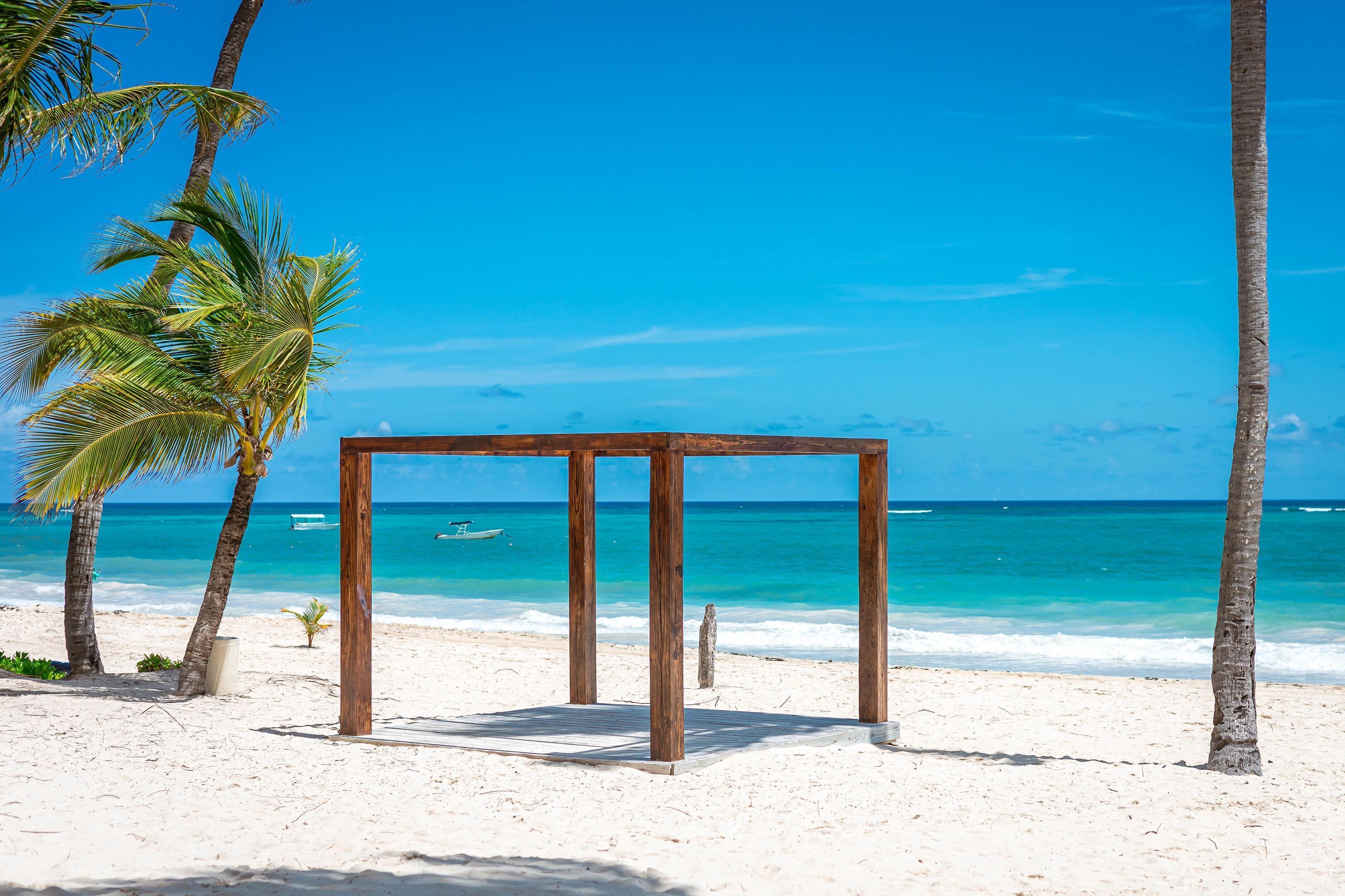 Eine Holzhütte an einem sandigen Strand mit klarem, blauem Wasser und Palmen.