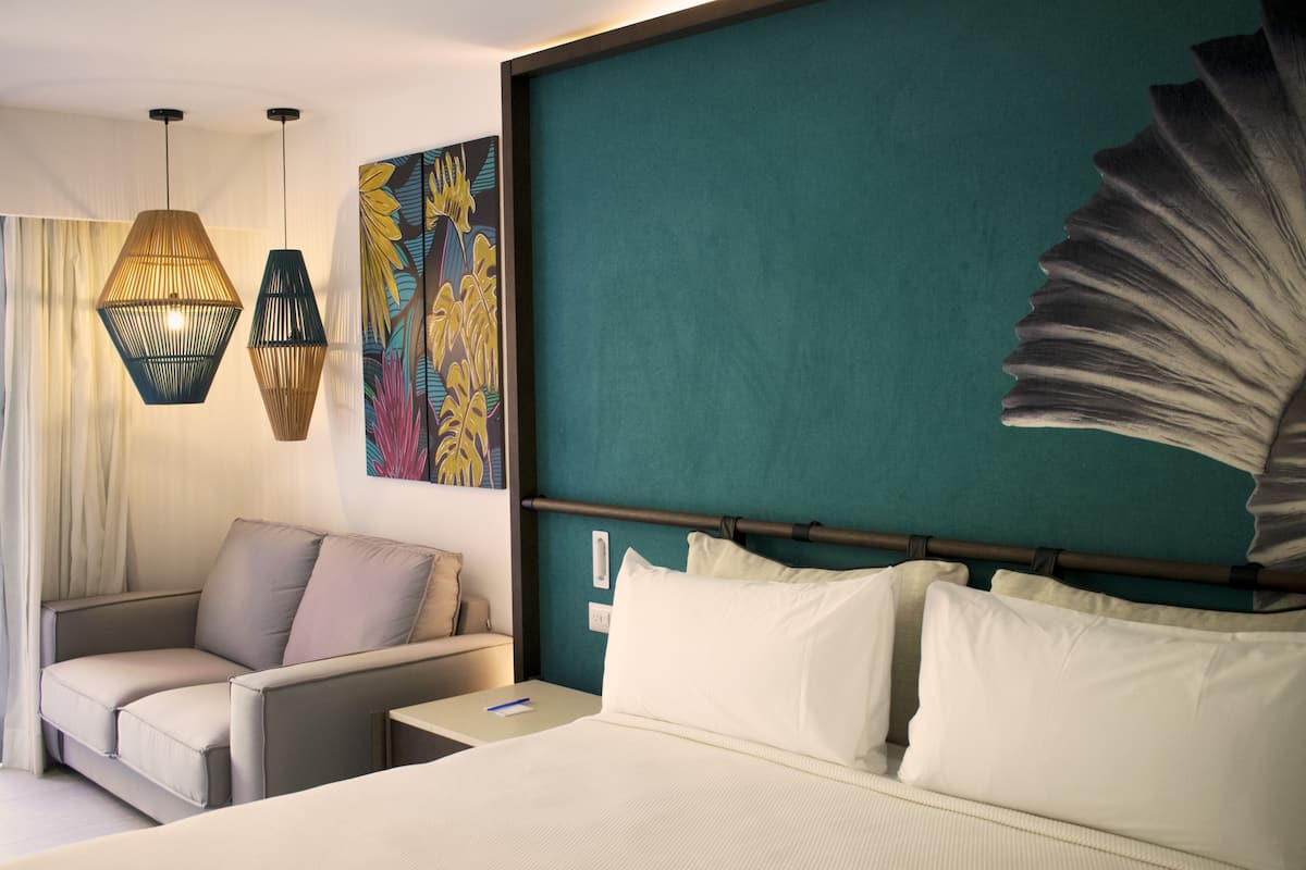 A hotel room with a bed, a sofa, a nightstand, and a wall with a large decorative piece.