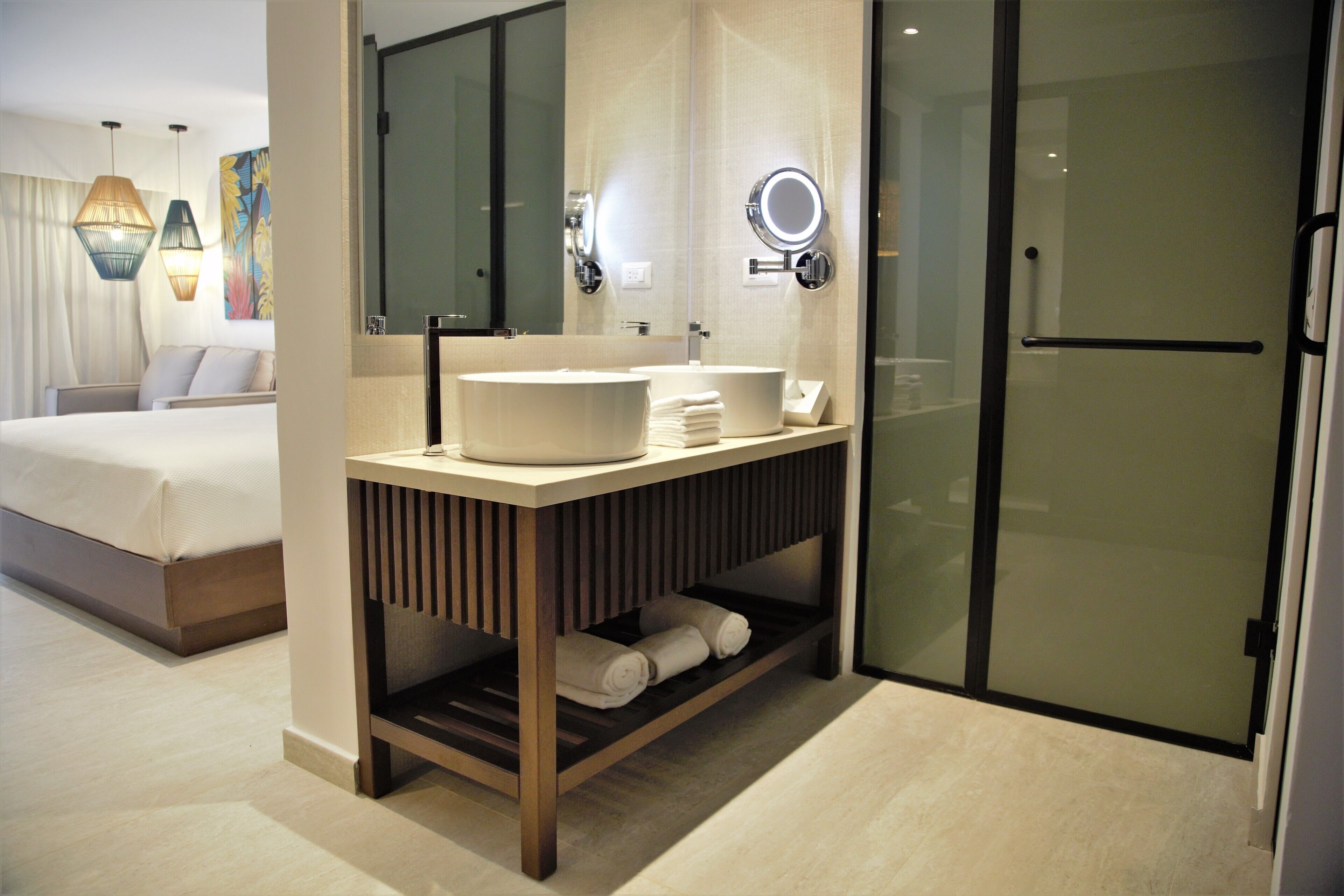 Un baño de hotel moderno con un espejo grande, un lavamanos y una puerta de ducha de vidrio.