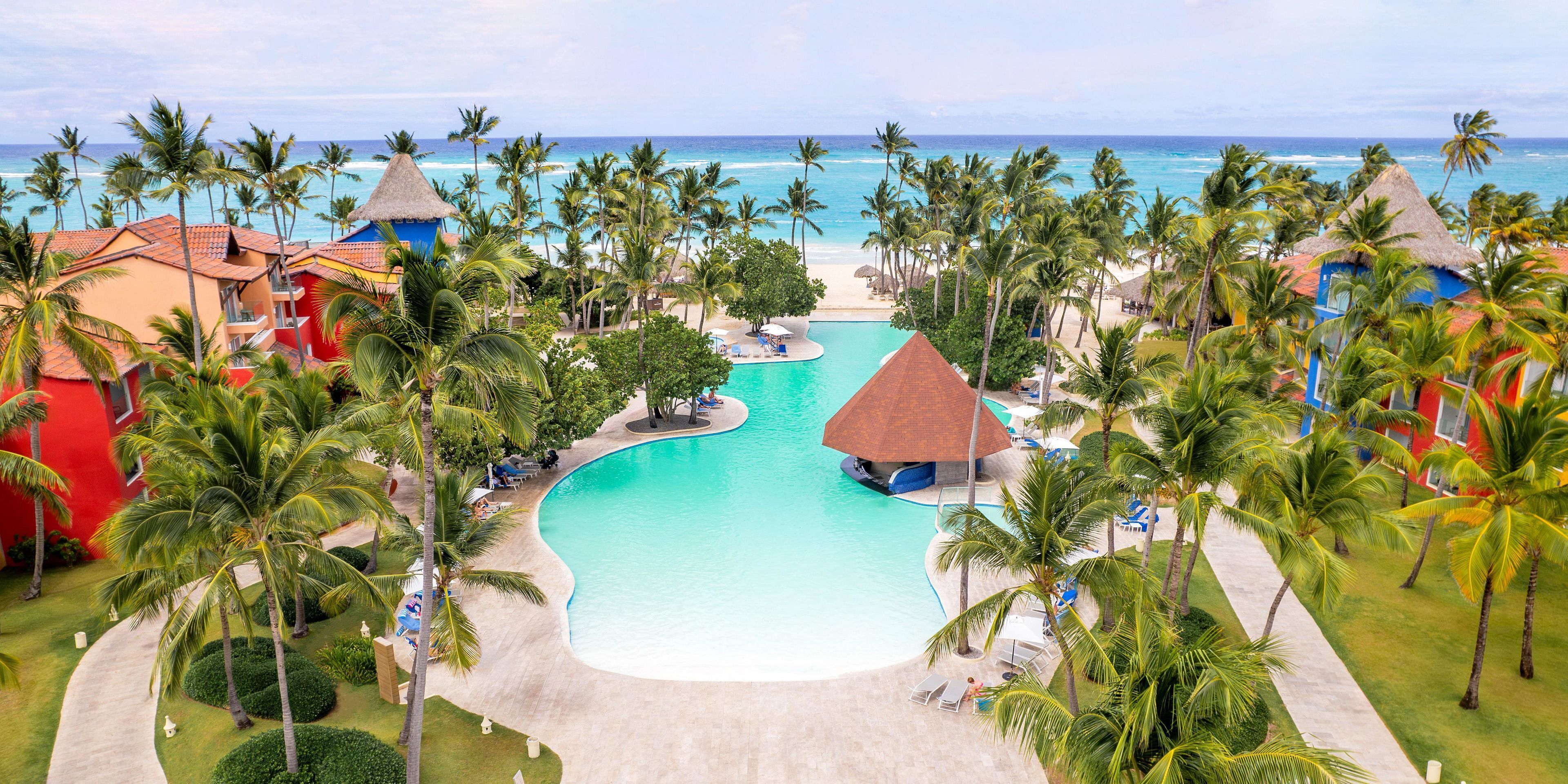 Un resort con una piscina grande, palmeras y vista a la playa.