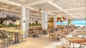A spacious indoor dining area with high ceilings, exposed beams, and a view of the beach.
