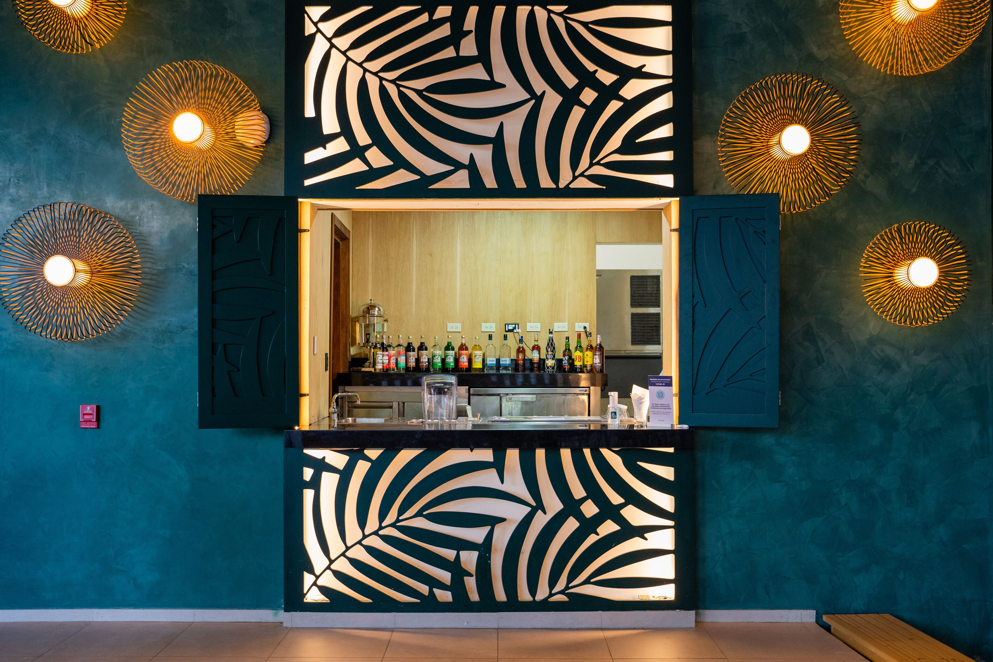 Zona de bar con barra central, estantes llenos de botellas e iluminación decorativa en la pared.