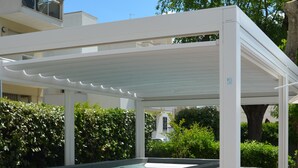 A covered outdoor swimming pool with steps leading into it, surrounded by greenery and a white building in the background. - Oxygen Lifestyle Hotel  (Rimini)