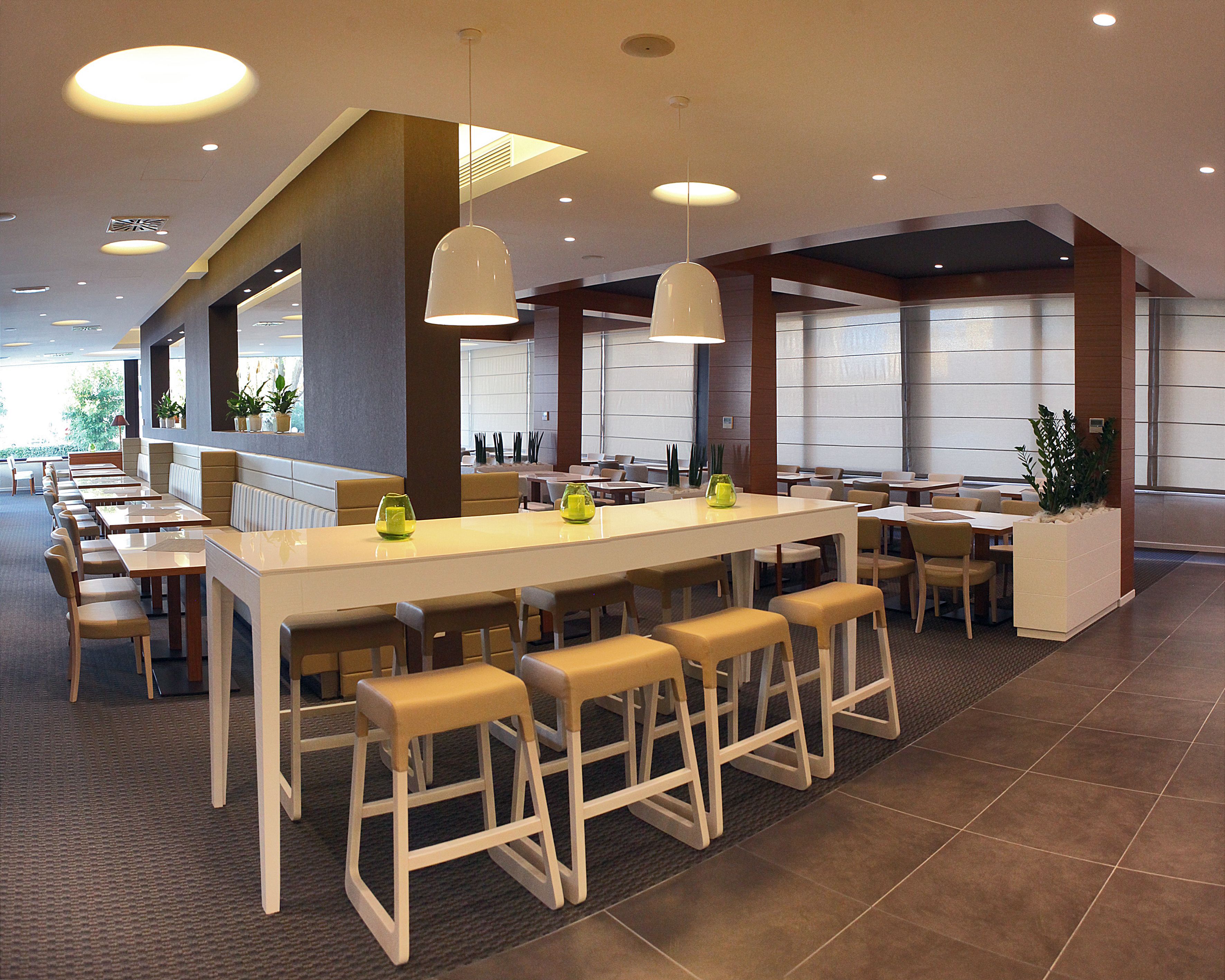 A modern restaurant with a long communal table, high ceilings, and pendant lighting.