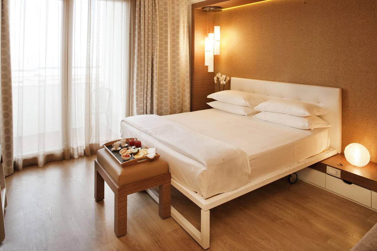 A hotel room with a bed, bedside table, and a tray with breakfast items.