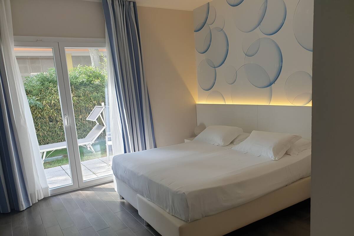 A modern bedroom with a large bed, a sliding glass door to a balcony, and a wall with a circular pattern.